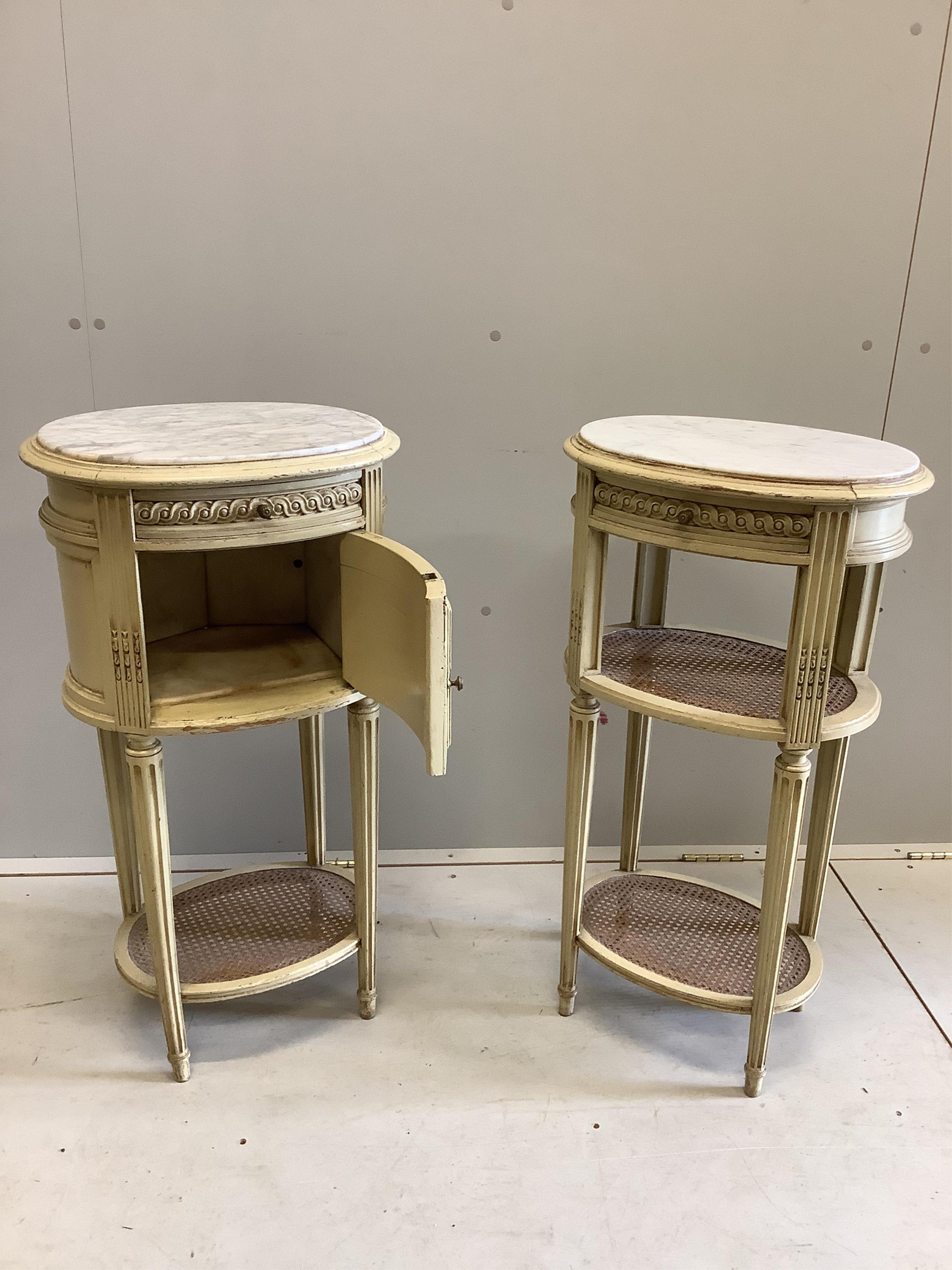 A pair of French cream painted bedside cabinets with oval marble inset tops, one fitted with a pot cupboard, width 44cm, height 83cm. Condition - fair, some differing to the marble